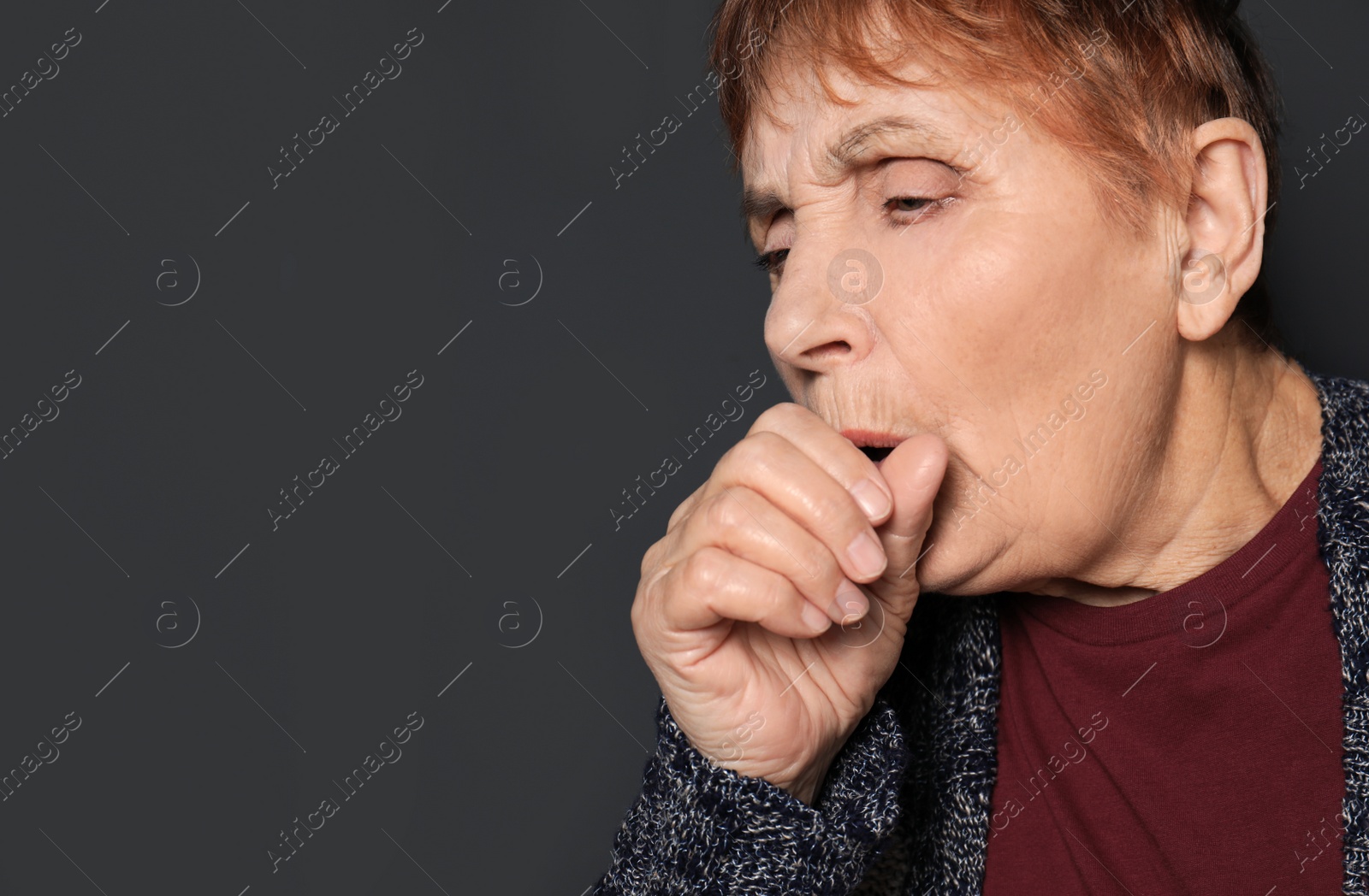 Photo of Elderly woman coughing against dark background. Space for text