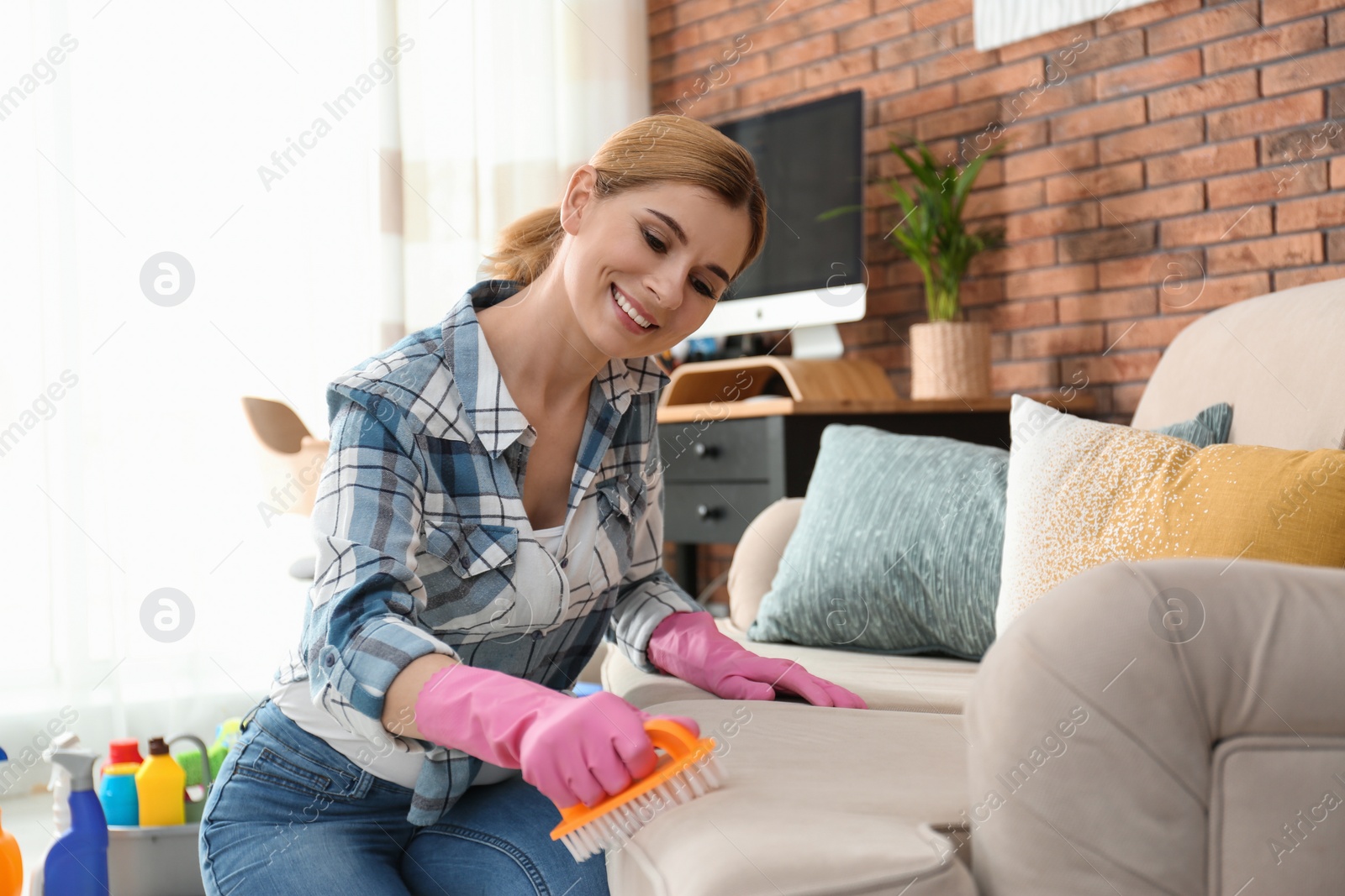 Photo of Portrait of woman cleaning sofa with brush in living room