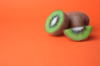 Photo of Whole and cut fresh kiwis on orange background, space for text