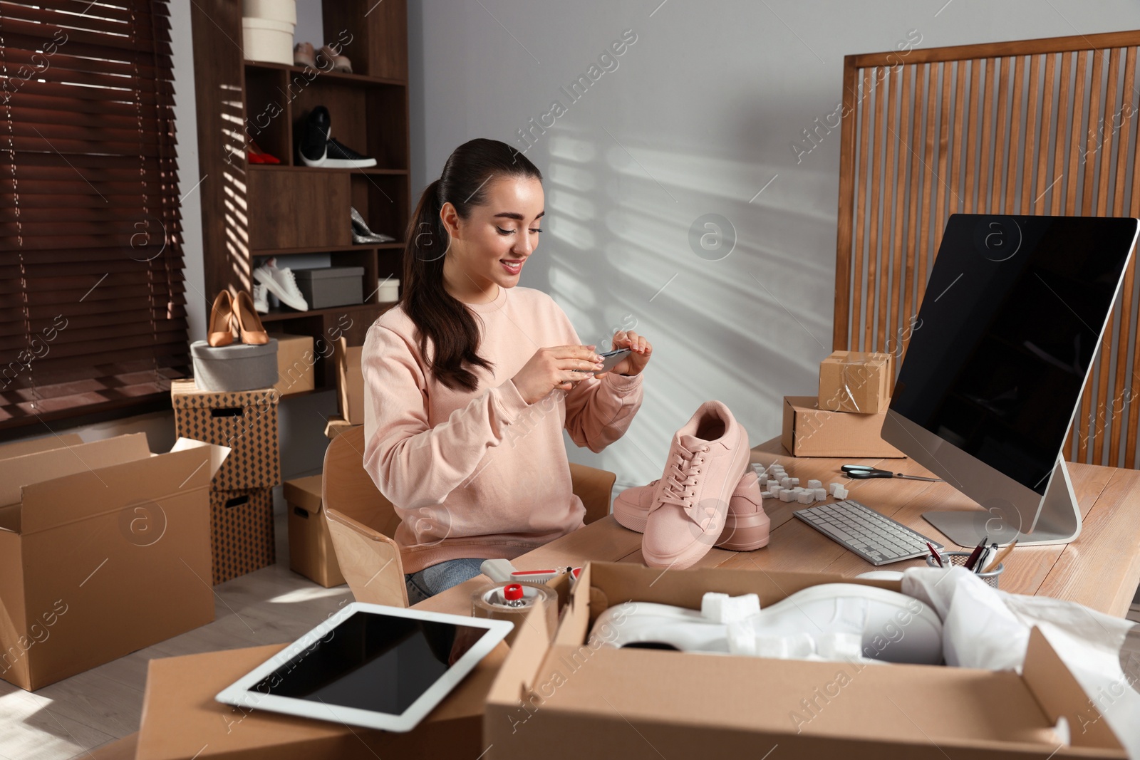 Photo of Shoes seller taking picture of pink sneakers at table in office. Online store