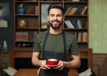 Portrait of barista with cup of coffee in shop