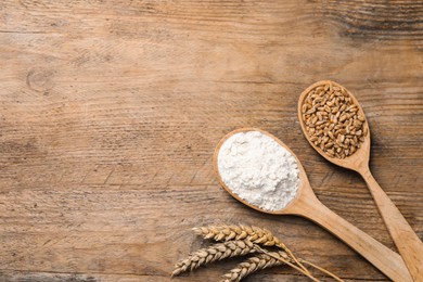 Spoons with wheat flour, grains and spikes on wooden table, flat lay. Space for text