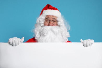 Photo of Santa Claus holding blank poster on light blue background. Space for text