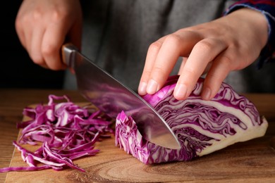 Photo of Woman cutting fresh red cabbage at wooden table, closeup