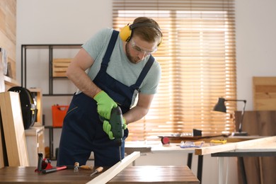 Carpenter working with electric drill at table indoors. Space for text