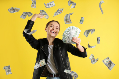 Happy young woman with dollars under money rain on yellow background