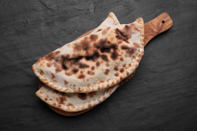 Photo of Wooden board with delicious calzones on black table, top view