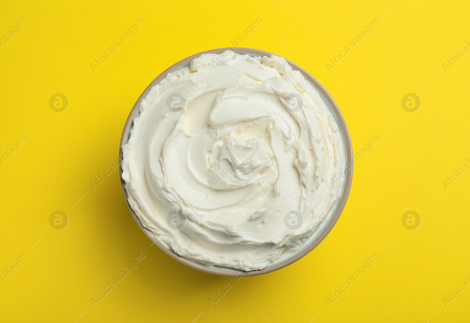 Photo of Bowl of tasty cream cheese on yellow background, top view