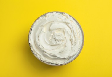 Photo of Bowl of tasty cream cheese on yellow background, top view