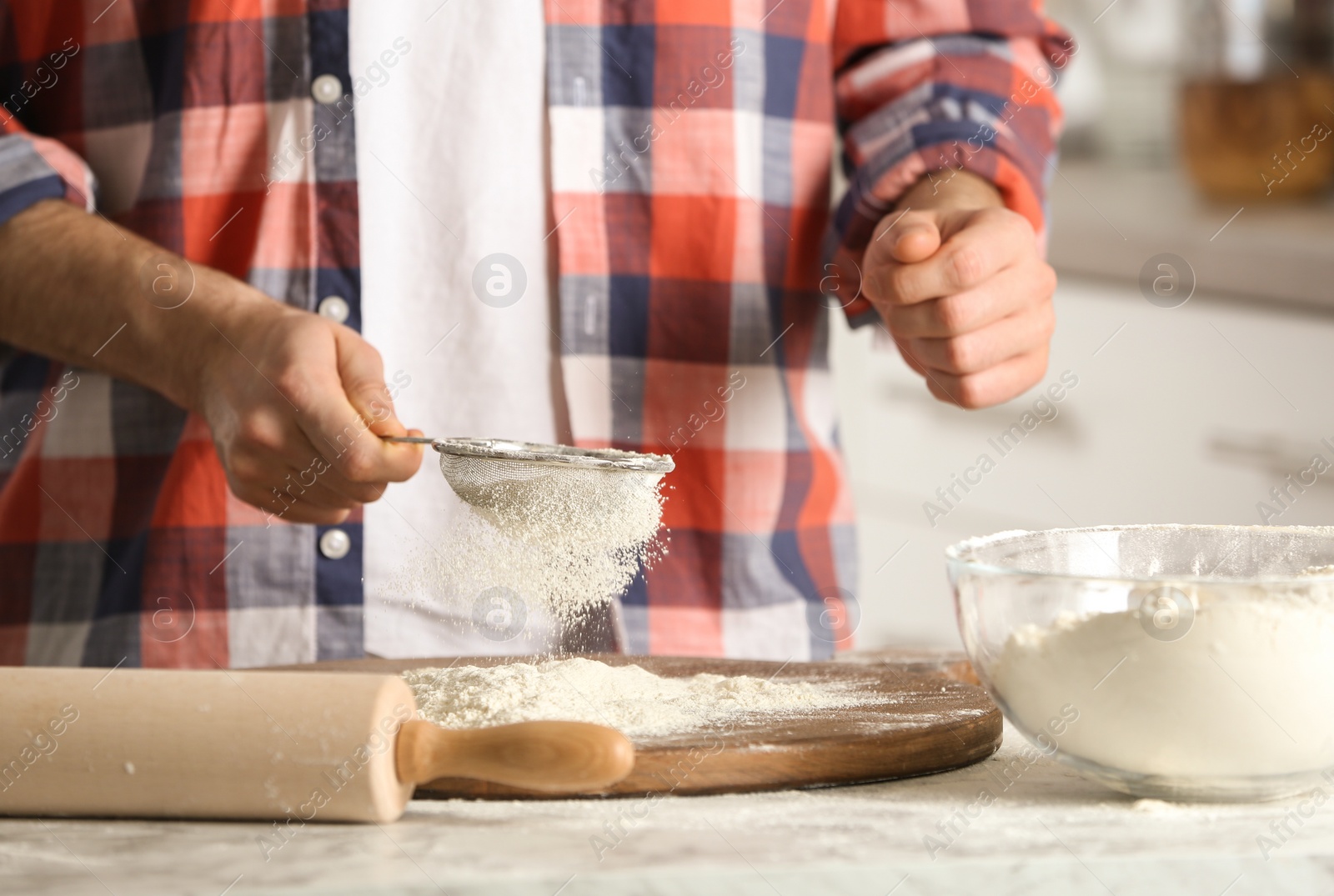 Photo of Man sprinkling flour over board on table in kitchen