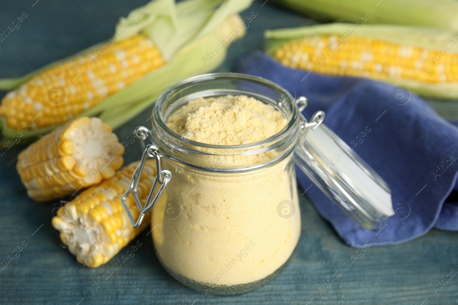 Photo of Corn flour in glass jar and fresh cobs on blue wooden table