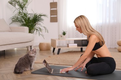 Photo of Beautiful woman with her cat watching online yoga class at home