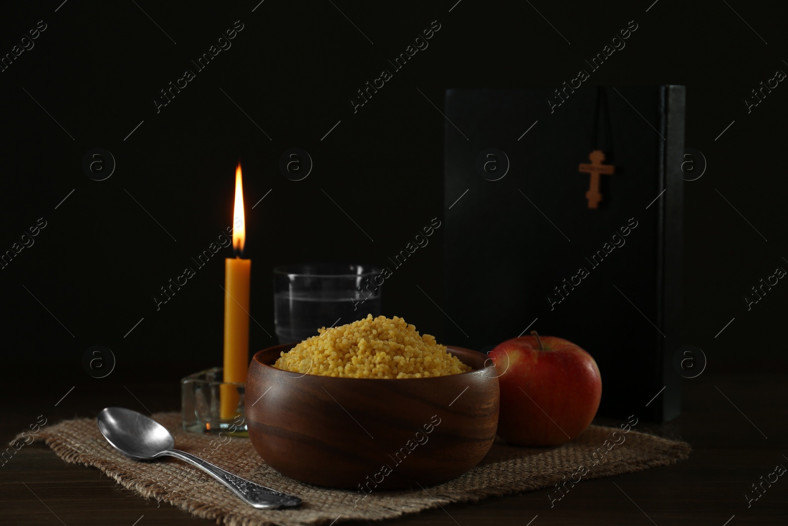 Photo of Millet, apple, water, burning candle, Bible and crucifix on wooden table. Great Lent season