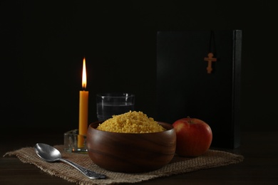 Millet, apple, water, burning candle, Bible and crucifix on wooden table. Great Lent season