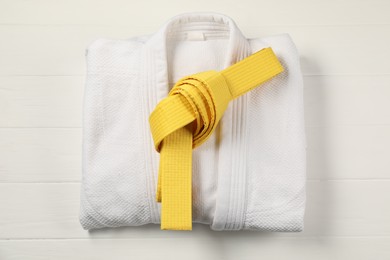 Yellow karate belt and white kimono on wooden background, top view