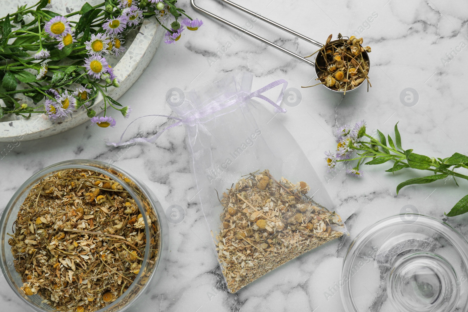 Photo of Scented sachet and dried chamomile flowers on white marble table, flat lay