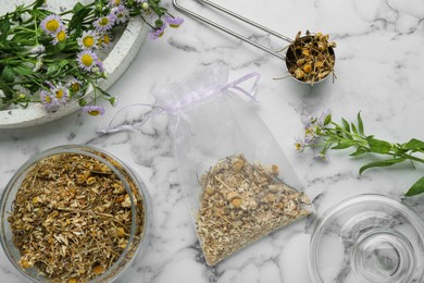 Scented sachet and dried chamomile flowers on white marble table, flat lay