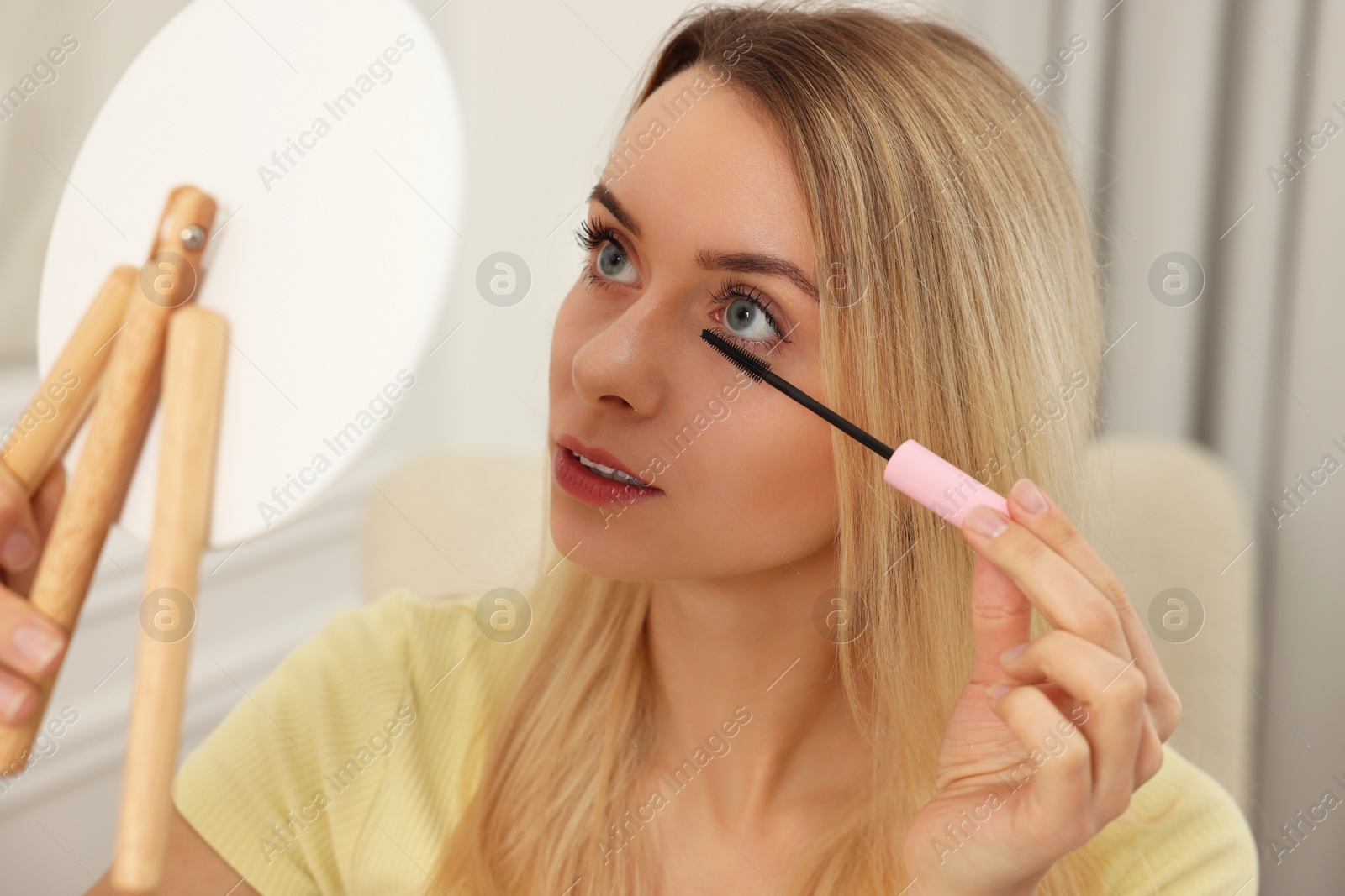 Photo of Beautiful woman with mirror applying mascara at home