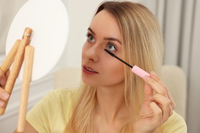 Beautiful woman with mirror applying mascara at home