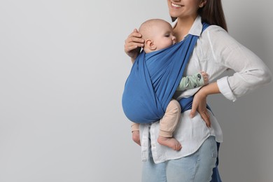 Photo of Mother holding her child in sling (baby carrier) on light grey background, closeup. Space for text