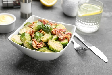 Photo of Delicious cooked Brussels sprouts with bacon served on grey table