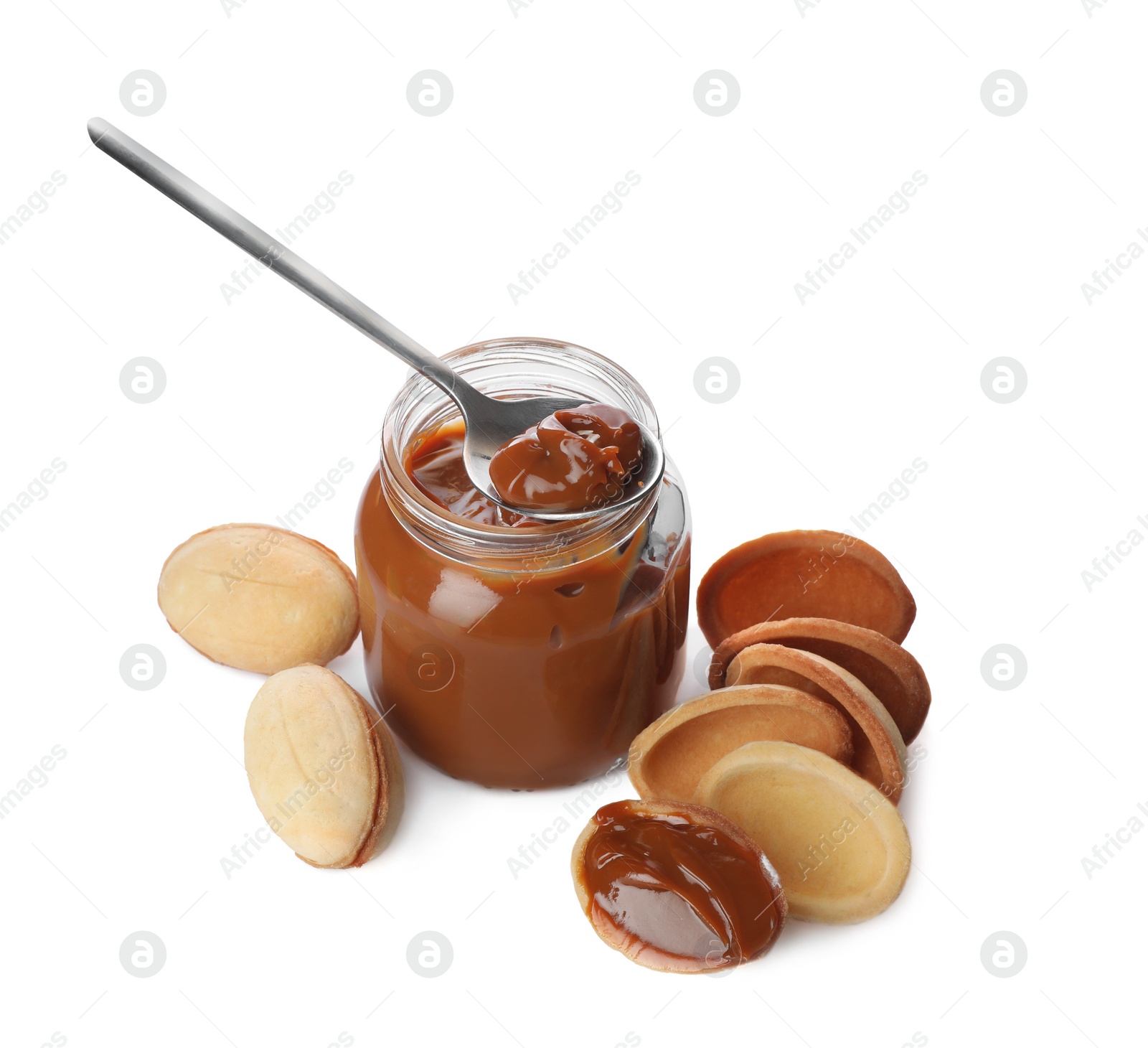 Photo of Jar with boiled condensed milk, spoon, cooked dough and walnut shaped cookies on white background