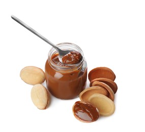 Photo of Jar with boiled condensed milk, spoon, cooked dough and walnut shaped cookies on white background