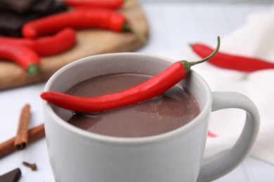 Cup of hot chocolate with chili pepper on white tiled table, closeup