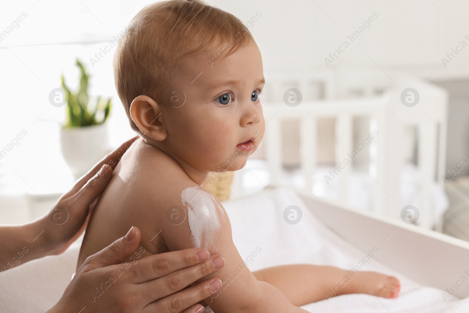 Photo of Mother applying body cream on her little baby at home, closeup