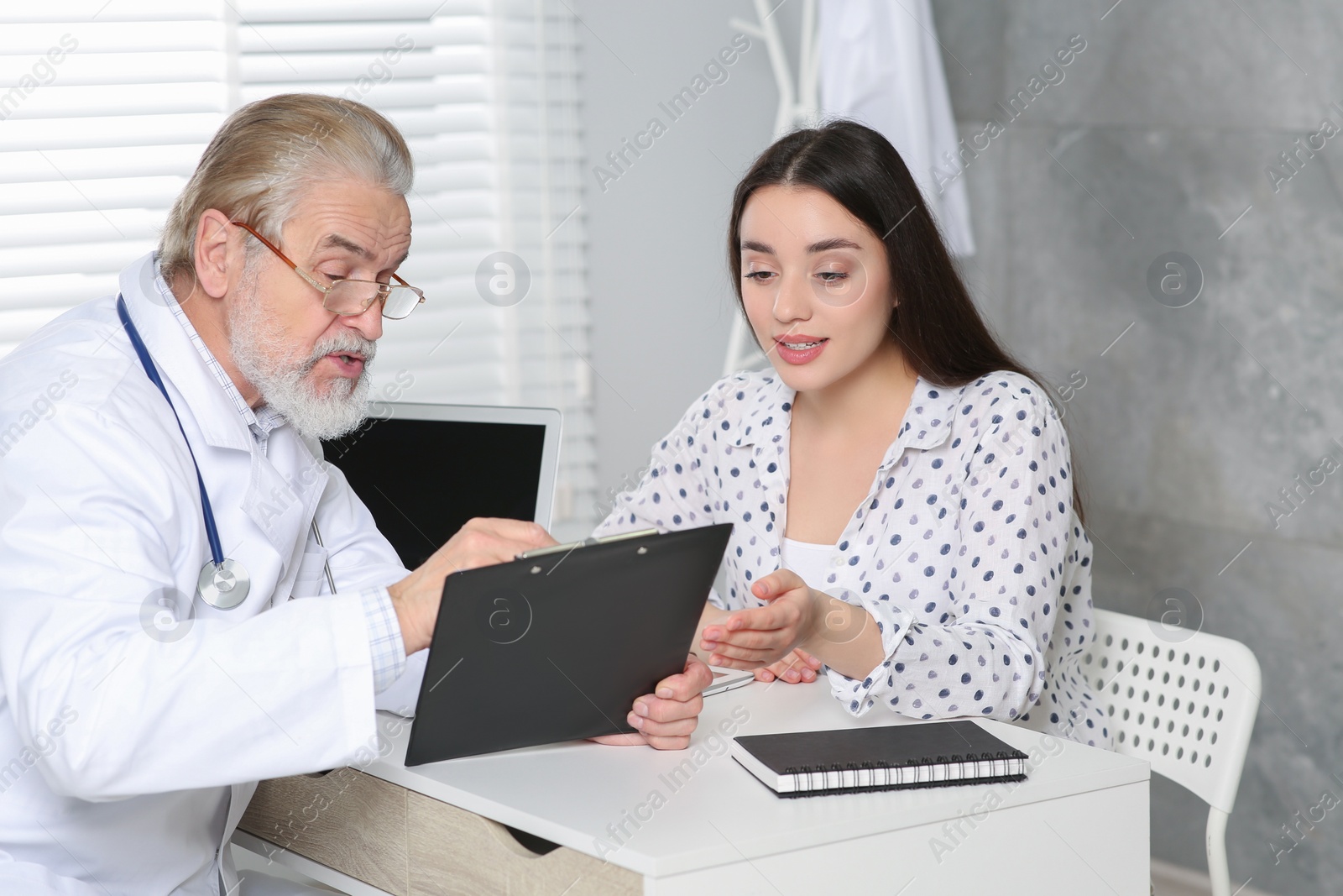 Photo of Senior doctor consulting patient at white table in clinic