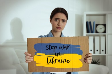Image of Unhappy young woman holding sign with phrase Stop War in Ukraine on sofa indoors