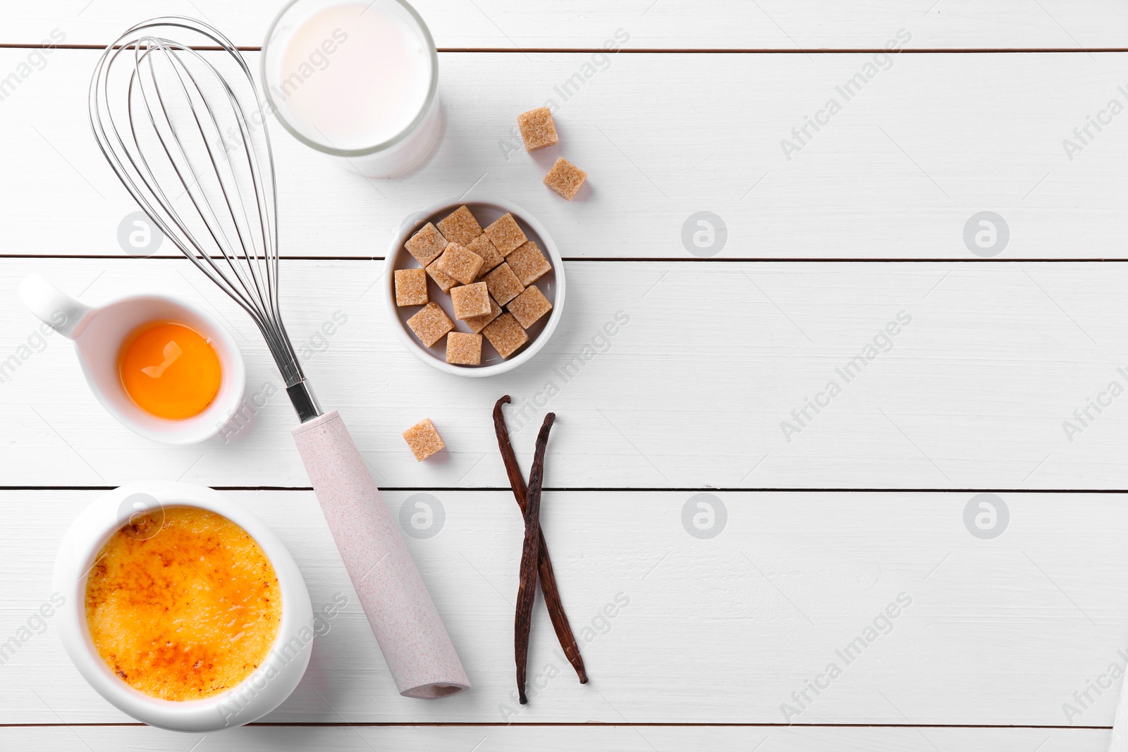 Photo of Delicious creme brulee in bowl and ingredients on white wooden table, flat lay. Space for text