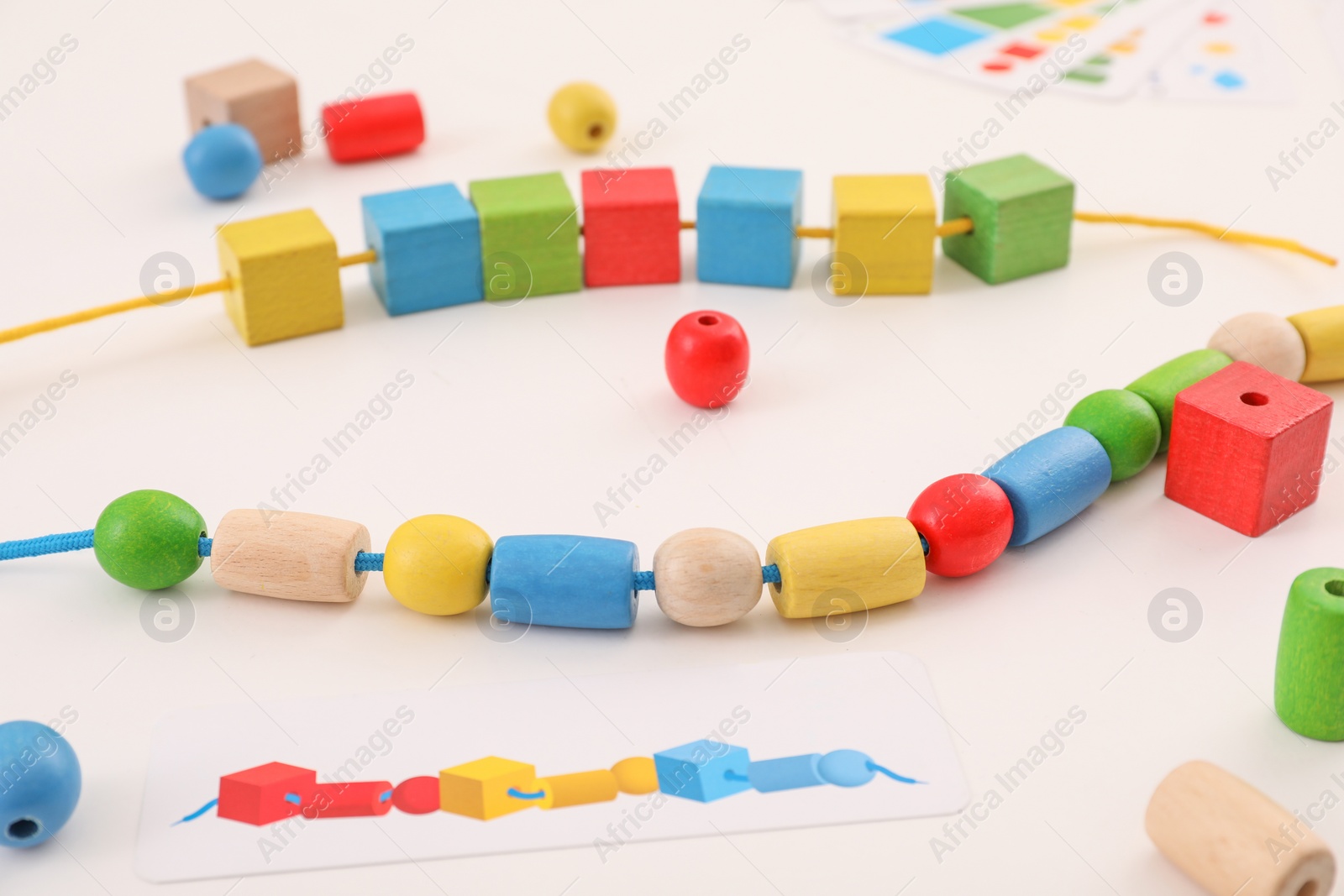 Photo of Wooden pieces and string for threading activity on white table. Motor skills development