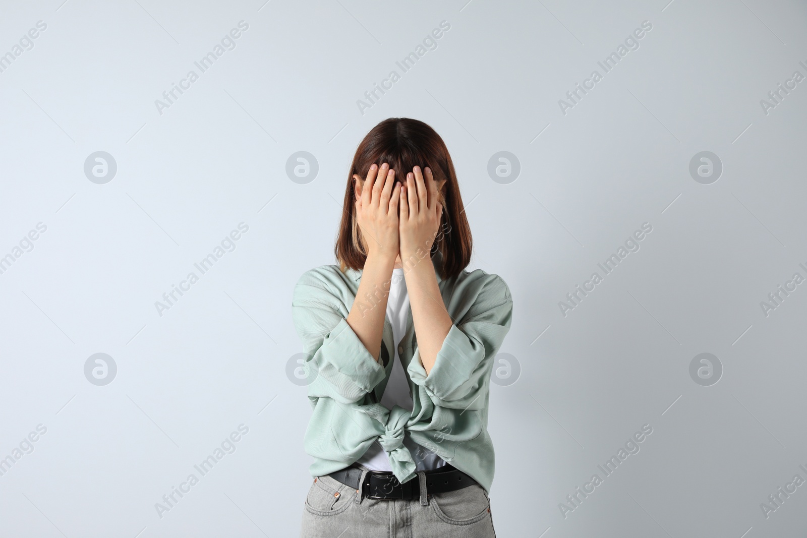 Photo of Young girl hiding face in hands on white background