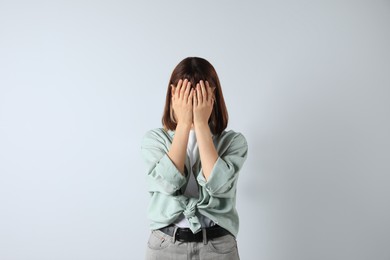 Photo of Young girl hiding face in hands on white background