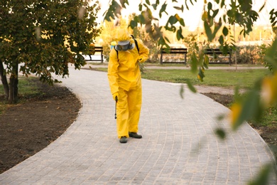 Photo of Person in hazmat suit disinfecting street pavement with sprayer. Surface treatment during coronavirus pandemic