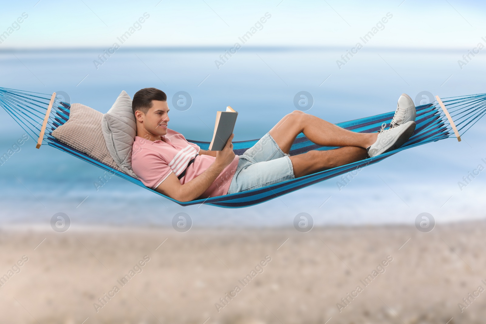 Image of Man reading book in hammock near sea on sunny day 