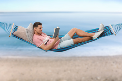 Man reading book in hammock near sea on sunny day 