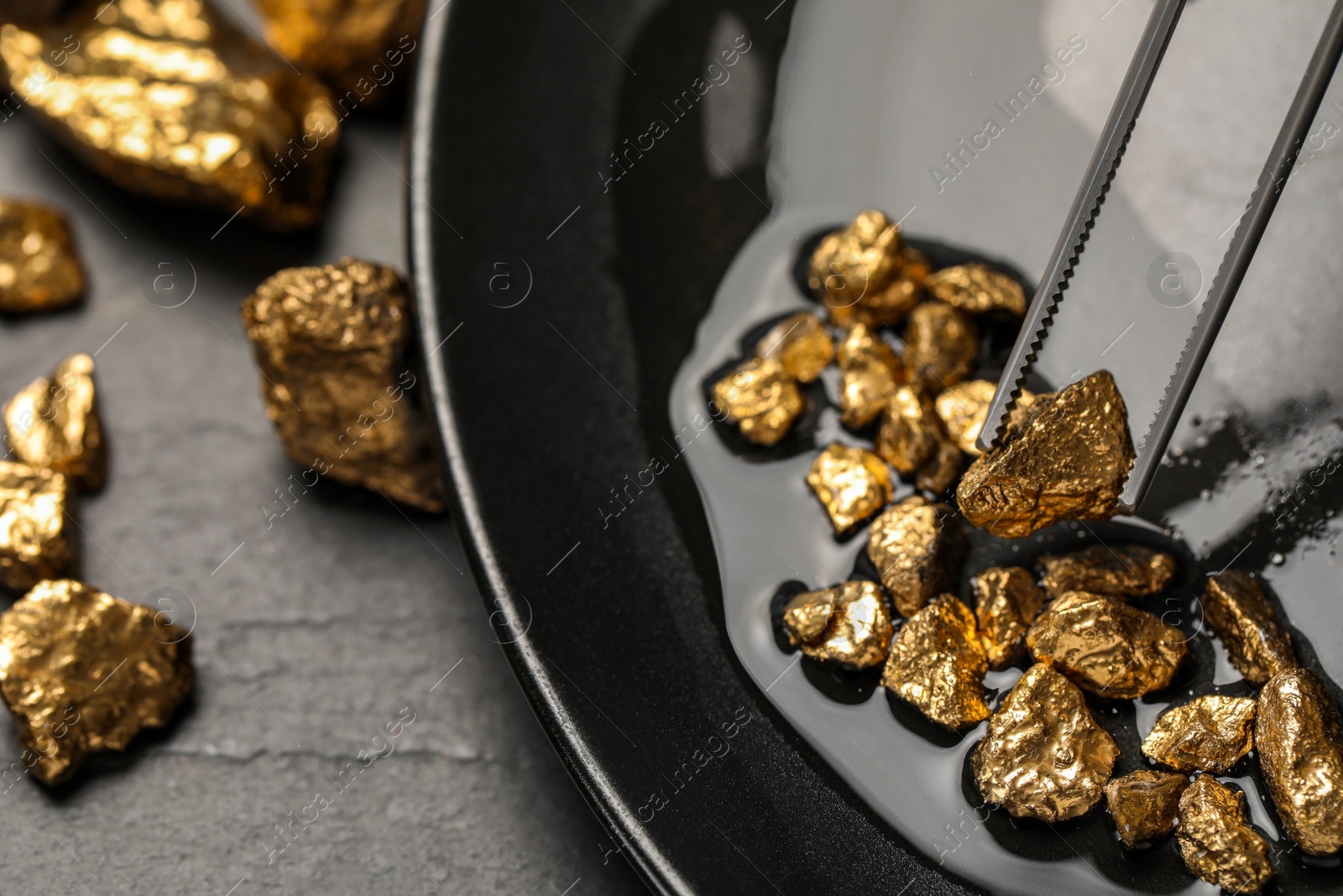 Photo of Tweezers with gold nugget above pile on black table