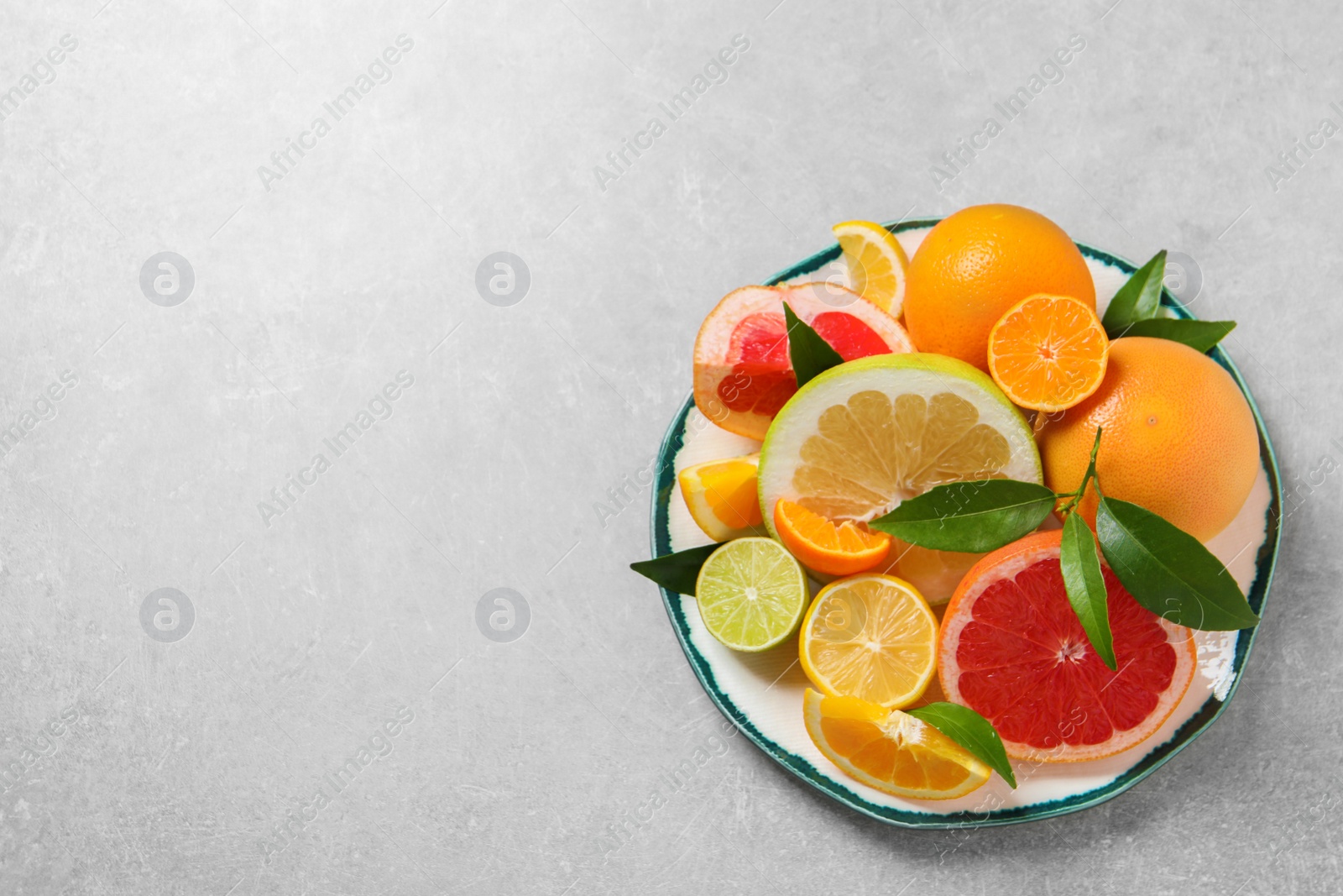 Photo of Plate with different citrus fruits and fresh leaves on light grey table, top view. Space for text