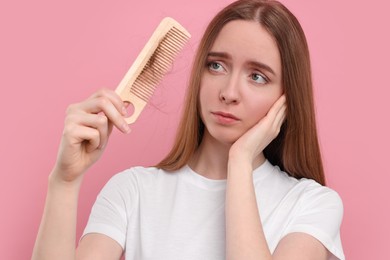 Photo of Woman holding comb with lost hair on pink background. Alopecia problem