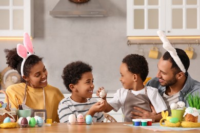 Happy African American family painting Easter eggs at table in kitchen