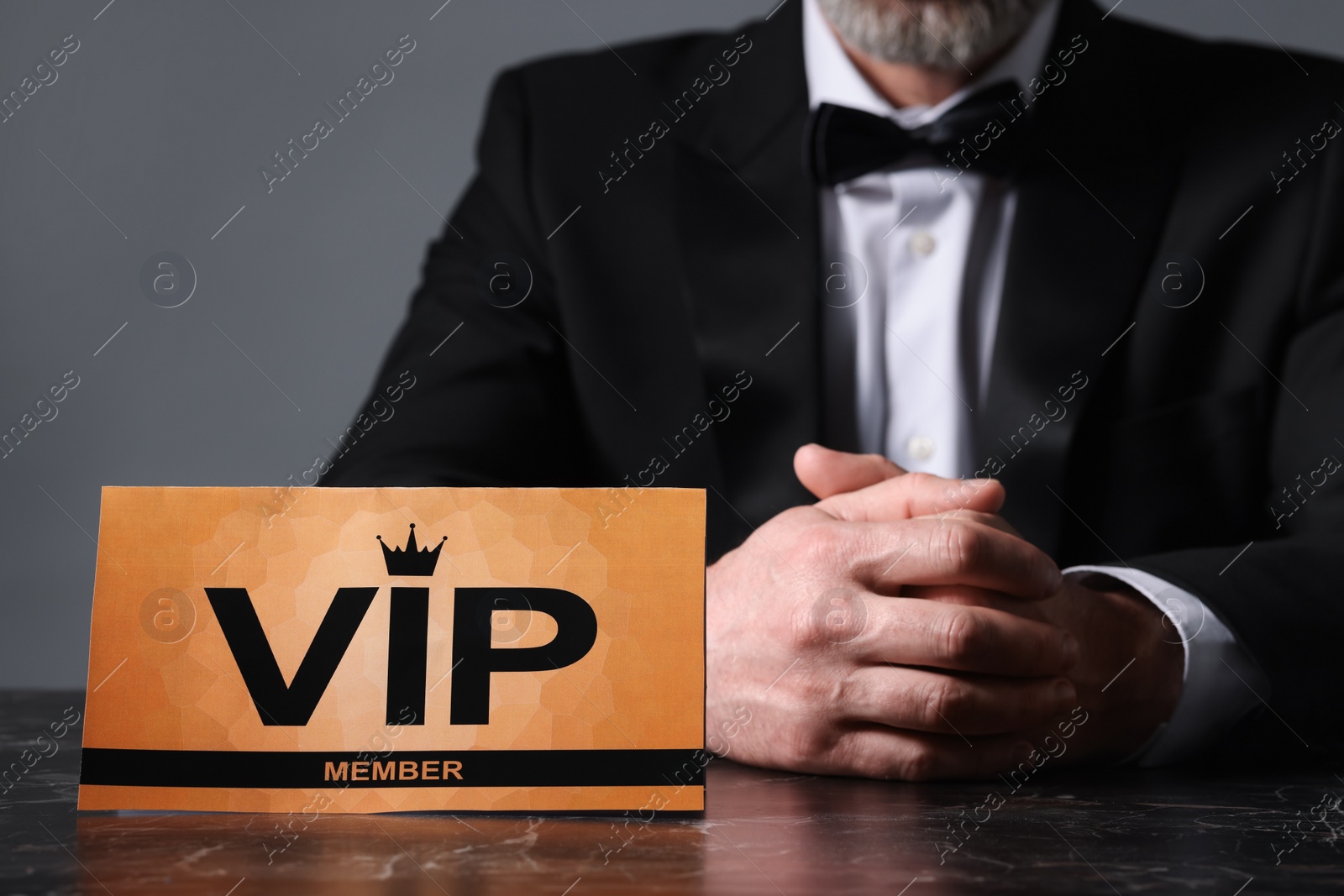 Photo of Man sitting at table with VIP sign on grey background, closeup