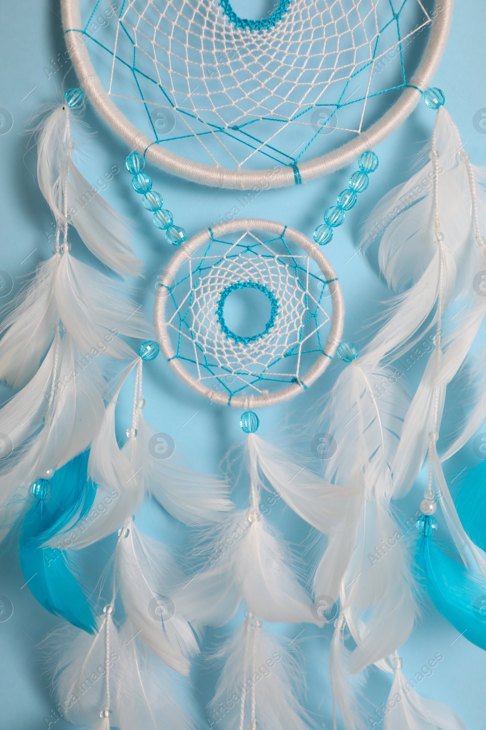 Photo of Beautiful dream catcher hanging on light blue background, closeup