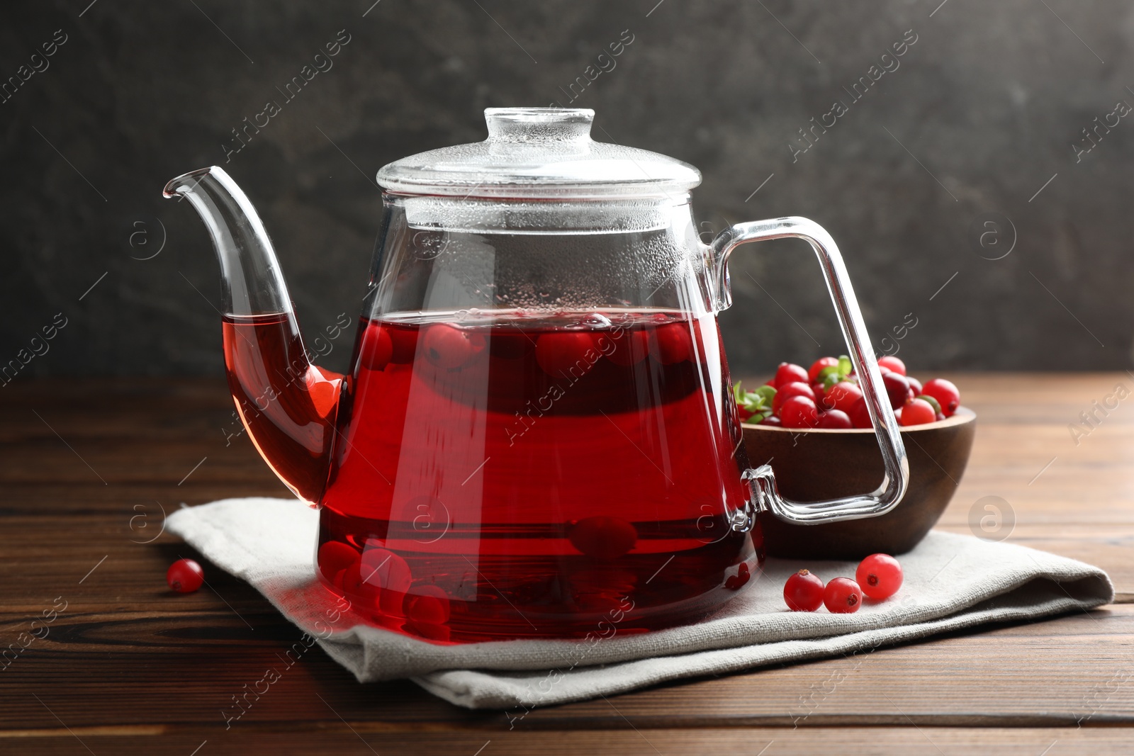 Photo of Tasty hot cranberry tea in teapot and fresh berries on wooden table