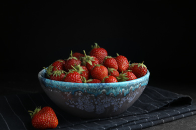 Photo of Delicious ripe strawberries in bowl on table against black background