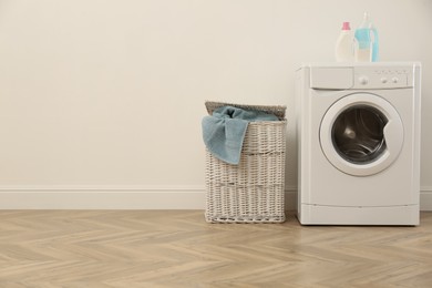 Photo of Laundry room interior with modern washing machine and wicker basket near white wall. Space for text