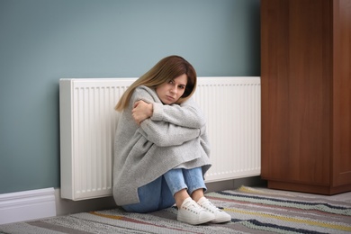 Sad woman suffering from cold on floor near radiator