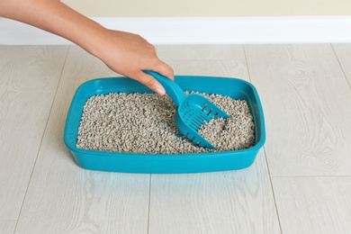 Woman cleaning cat toilet with scoop on floor. Pet care