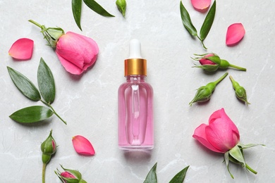 Flat lay composition with fresh flowers and bottle of rose essential oil on table